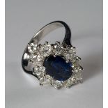 An 18ct white gold and sapphire ring, the mid-blue oval cut sapphire with a border of 12 round