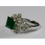 An 18ct white gold, emerald and diamond set ring, the square cut emerald mounted above diamond set