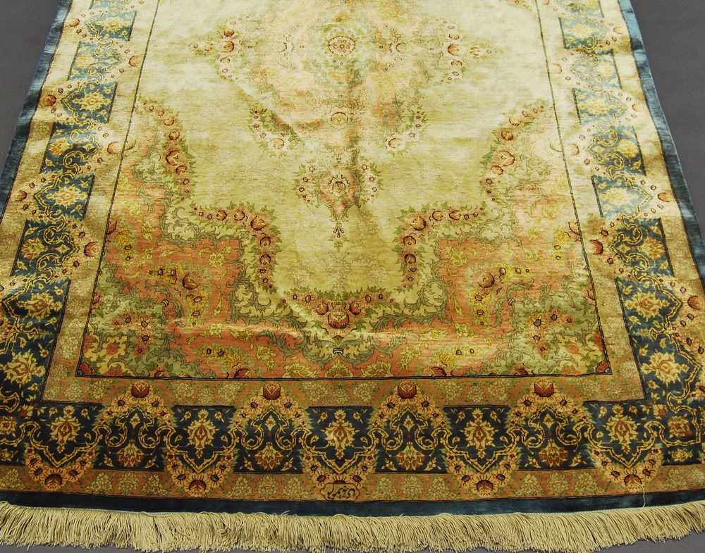 A Ghom silk rug, late 20th Century, with medallion in fawn coloured field within main blue border