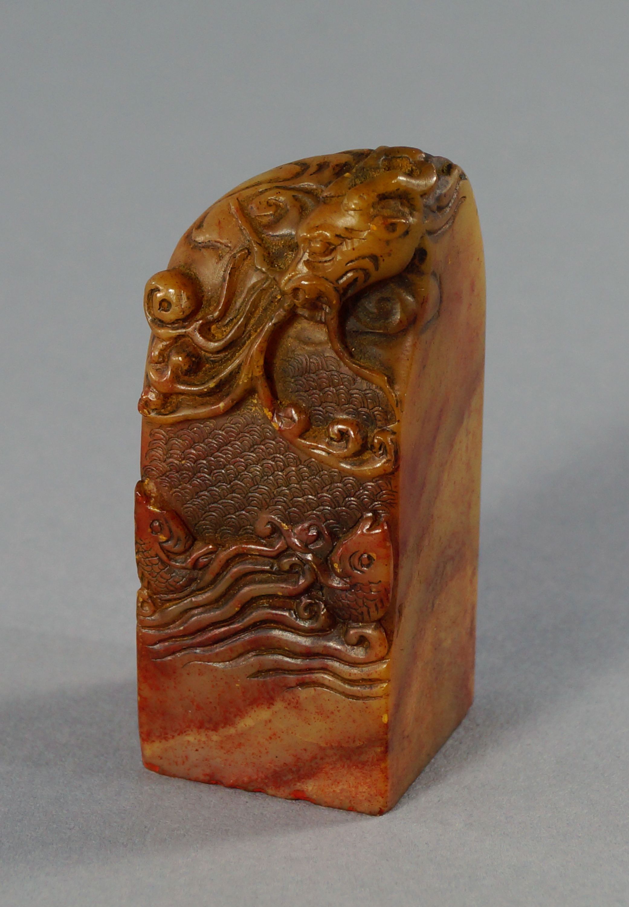 A Chinese soapstone seal, 20th century, carved to the top with a dragon above fish in the sea, 6cm