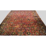 A Kirman carpet with all over foliate design in a wine coloured field and with stylised vine in an