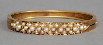 A late 19th/early 20th century unmarked gold, seed pearl set hinged bangle
The front with pierced