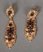 A pair of unmarked gold garnet set ear pendants
Of pierced scrolling form.  Each 6 cm high.