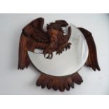 A BLACK FOREST WALL MIRROR, carved as an Eagle holding a crescent bevelled mirror.