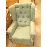 A Victorian style wing and button back arm chair upholstered in green floral fabric and raised on