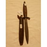 An early 20th C throwing knife in leather sheath having scrolled hilt and carved handle with brass