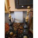 A pair of early 20th C black painted cast iron fire dogs with brass finials and roundals raised on