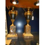 A pair of bronze urns having gilt mask handles resting on marble plinth base