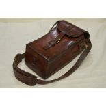 Leather magazine carrier with hinged buckle top of curved form with hanging shoulder strap