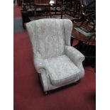 A Parker Knoll Wing Back Easy Chair, patterned brocade, raised on brass castors.