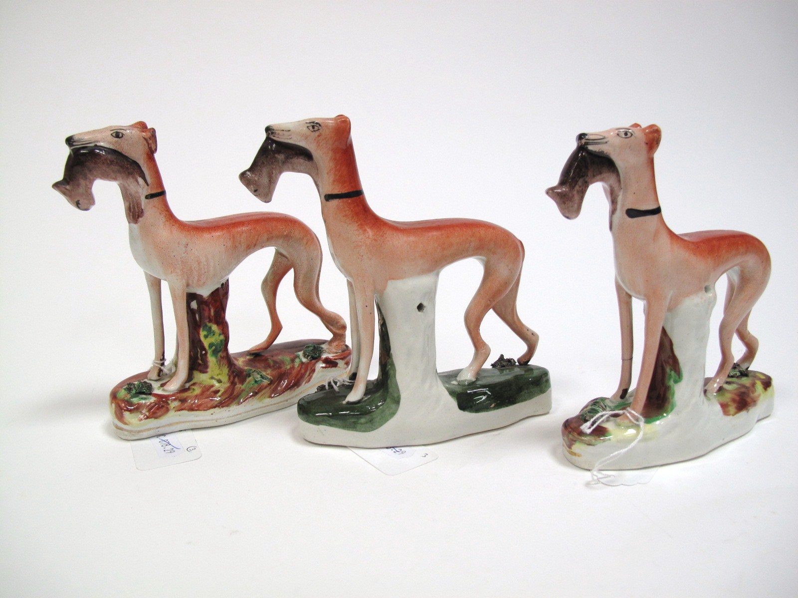 A Pair of XIX Century Staffordshire Pottery Greyhound Dogs, each holding game, on naturalistic base,