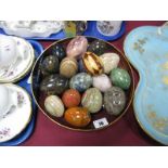 Alabaster, onyx, other mineral and wooden eggs, in glass bowl.