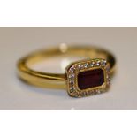 An 18ct gold ruby and diamond ring, the central baguette cut ruby surmounted 18 mili diamonds, (ring