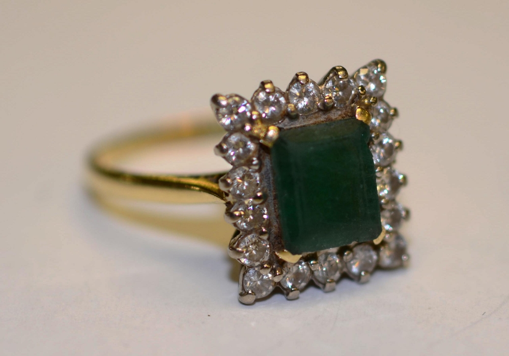 An 18ct gold emerald and diamond ring, the central baguette cut emerald, surrounded by 18 round
