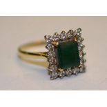 An 18ct gold emerald and diamond ring, the central baguette cut emerald, surrounded by 18 round