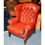 A red Chesterfield wingback armchair, with high sides and buttonback, cushion arm rests,