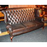 A brown leather button back three seater settee, with high back and sides, cushion arms, raised on