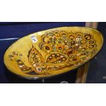 A Chelsea Pottery slipware dish, with peacock decoration glazed in brown and green on yellow ground,