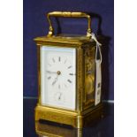 A brass embossed carriage clock, with carry handle and glazed top, the white dial with Roman