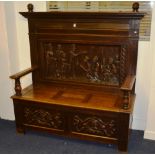 A carved oak hall settle, with turned finials to top above carved panel and hinged box seat,