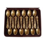 SET OF TWELVE GILDED SILVER SPOONS each with a pierced Celtic scroll silver handle and scalloped