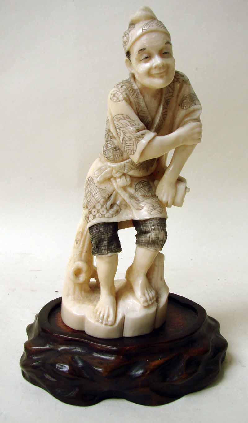 A Japanese carved ivory Okimono figure of a smiling man leaning on a branch and holding a pouch,