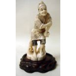 A Japanese carved ivory Okimono figure of a smiling man leaning on a branch and holding a pouch,