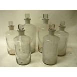 A selection of six clear glass pharmaceutical bottles with acid etched shield shape labels and