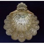 A George V silver bon bon dish of embossed shell shape with acanthus leaf handle, supported on three