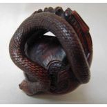 A Japanese carved wood netsuke as a serpent emerging from a pair of stylised dragons with a pearl,