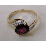 A modern 9ct gold garnet and diamond cross over ring, the large central oval 10mm by 7mm garnet