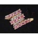 A modern 9ct gold pink sapphire and diamond cross over ring, three strands of sapphires