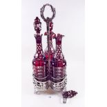 A Victorian silver plated decanter stand with central ring handle, fitted three Bohemian red flashed