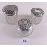 Three cut glass and silver topped toiletry jars with embossed decoration