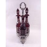A Victorian silver plated decanter stand with central ring handle, fitted three Bohemian red flashed