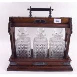 An Edwardian oak three bottle tantalus with silver plated mounts, with key