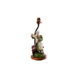 A continental porcelain figural lamp base, AF, modelled as a seated lady with a sewing box, with
