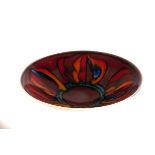 A Poole pottery Aegean dish, decorated with bright red, orange and blue petal shapes, on dark red