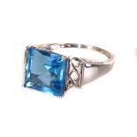 A 9K white gold and topaz dress ring, the square cut blue stone set in four claw mount, with pierced