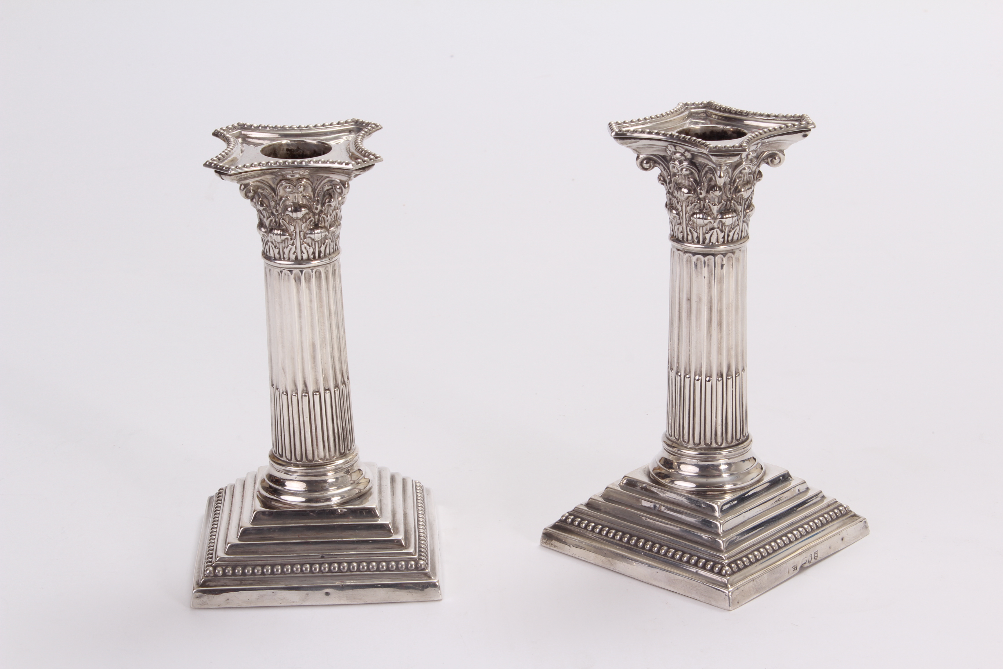 A pair of late Victorian silver filled candlesticks by Edward Hutton, having square bases supporting