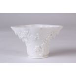 An 18th century blanc-de-chine libation cup, styled as a rhinoceros horn with cameo prunus and