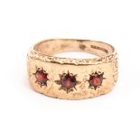 A vintage 9ct gold and three stone garnet ring, the thick tablet with scroll sides and set with