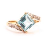 A yellow metal and gem set dress ring, having a large square cut blue stone in crossover style mount