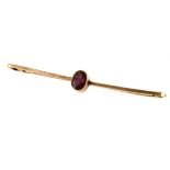A 9ct gold and ruby stick pin/bar brooch, the oval cut ruby centrally mounted in rubbed over