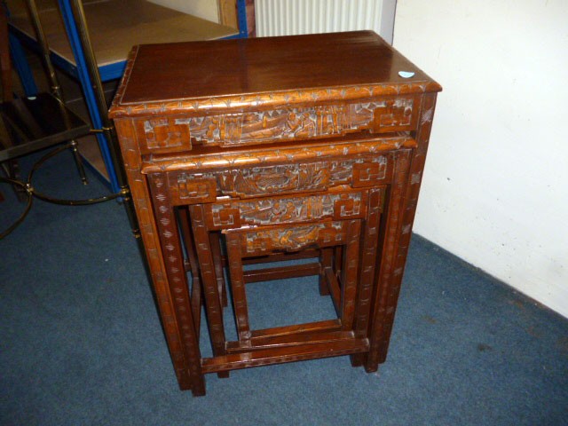 A nest of four Chinese hardwood tables, having carved oriental scenes to side, with lower stretcher