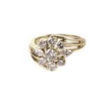 A modern diamond cluster ring, the crossover style yellow metal mount having a flower head style