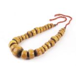 A large rare antique amber bead necklace, made up of graduating thick discs of toffee opaque amber