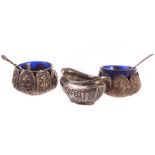 A pair of Indian white metal salt cellars, with flowers in lozenges, blue glass liners, together