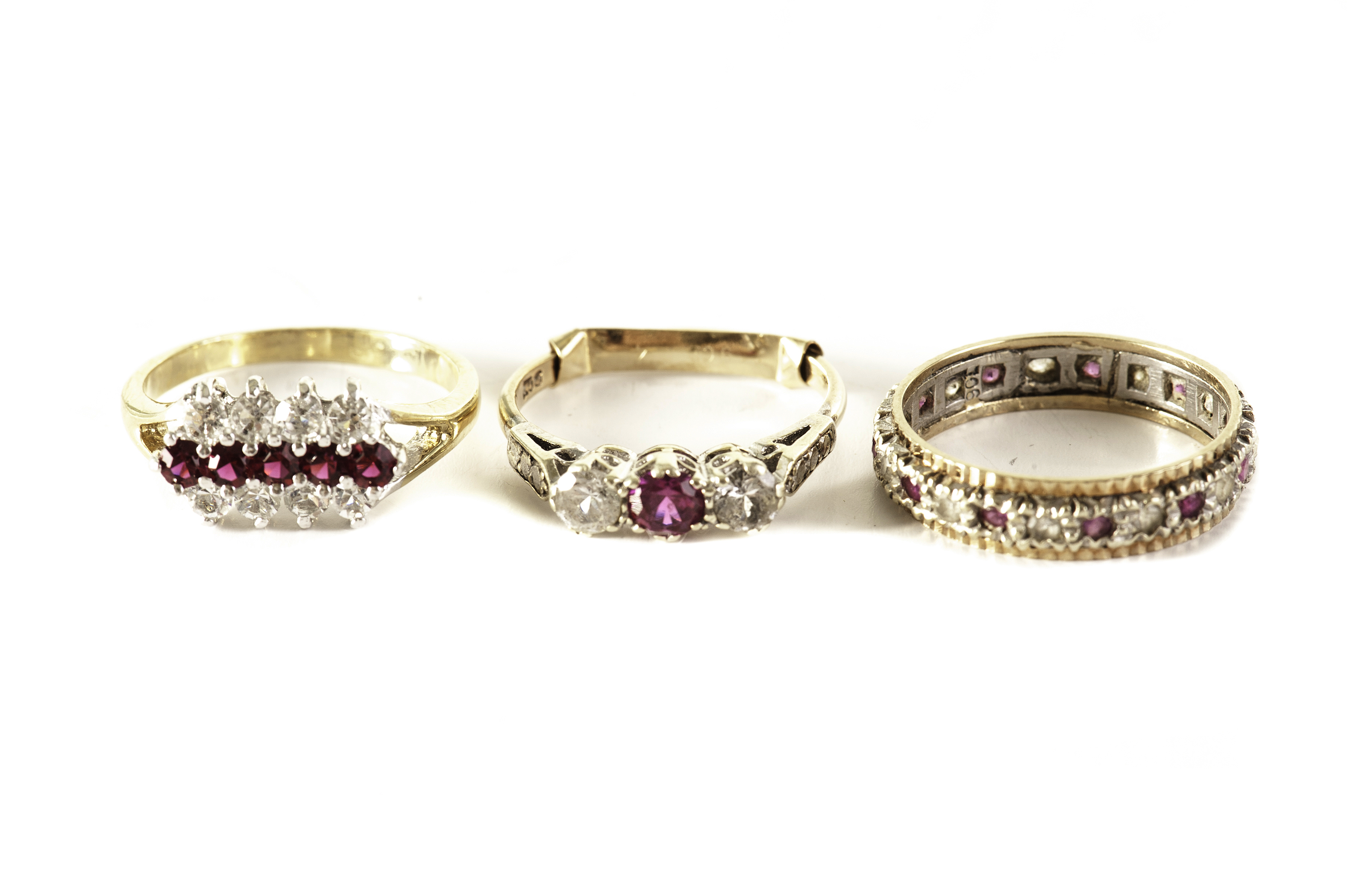 A group of three gem set dress rings, comprising an eternity ring, a three row cluster ring, and