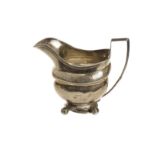 A Georgian period silver milk jug, helmet shaped having engraved designs, on four ball supports,